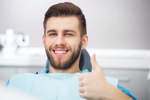 Man smiling sitting in dental chair giving a thumbs up sign