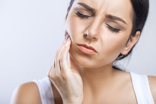 Woman grimacing with hand on jaw indicating she has a toothaceh