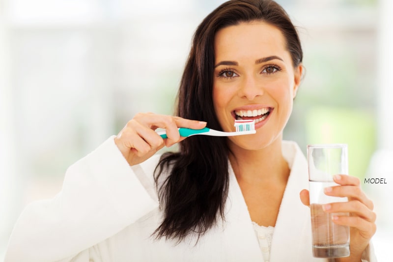 Woman holding toothbrush and glass of water