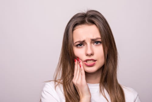 Woman grimacing while holding her hand against her jaw