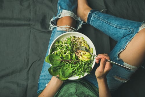 Person holding a bowl of leafy green vegetables