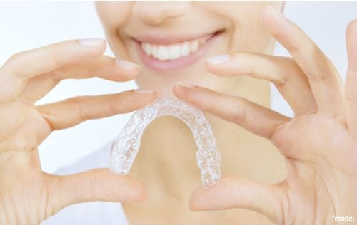 A woman smiles after getting her teeth whitened with custom-fit trays. 