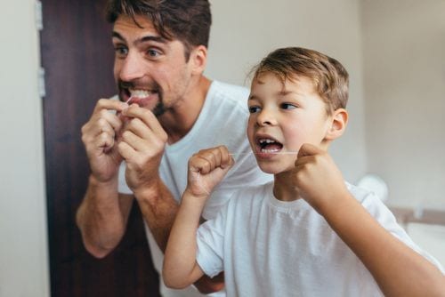 A father and son brush their teeth to avoid gingivitis and cavities. 