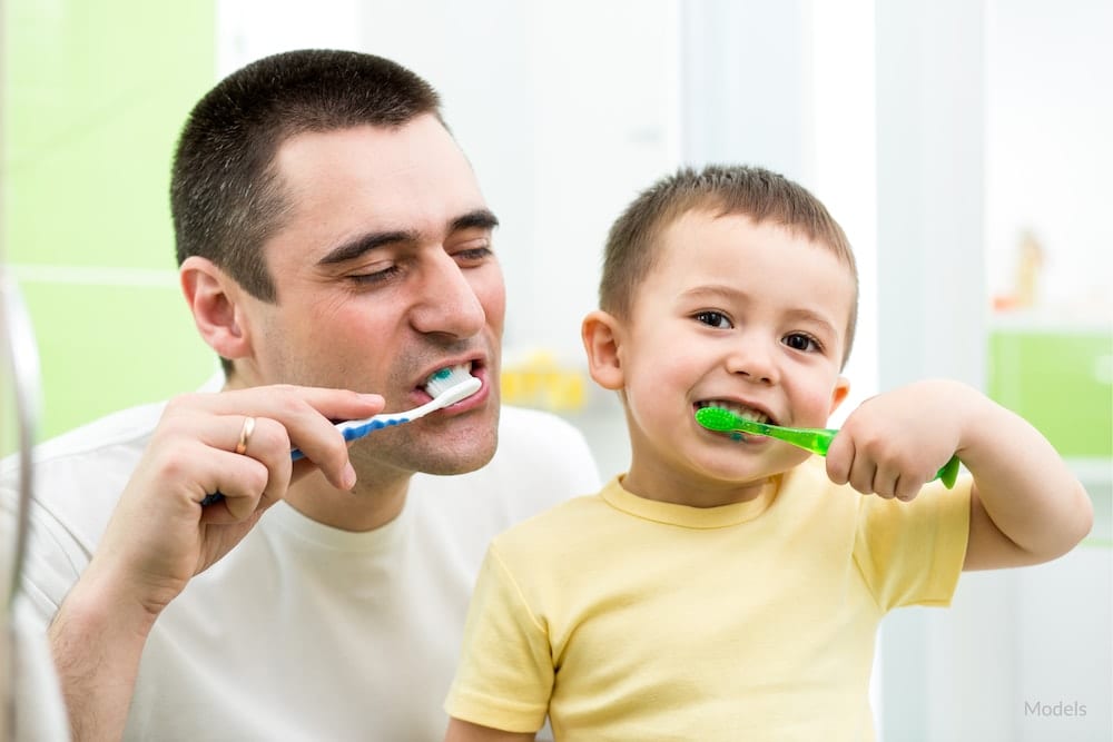 Father showing his son the right way to brush his teeth.