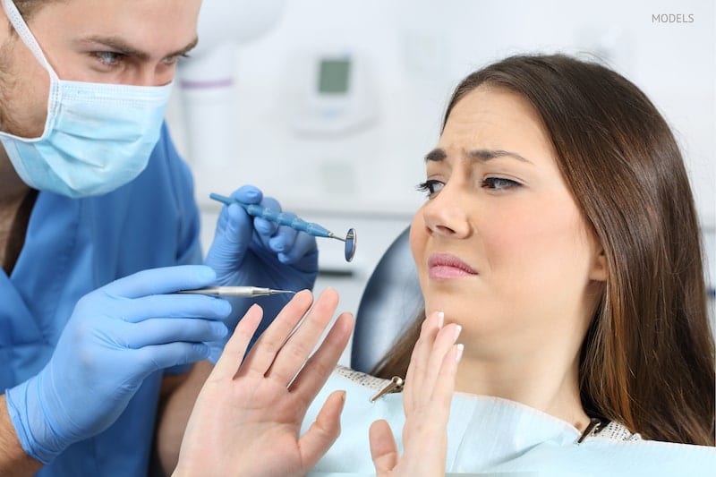 Scared patient sitting in the dental chair while the dentist is trying to examine her.