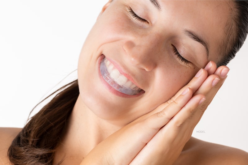 Women smiling and pretending to sleep, wearing a mouth guard against a white background.