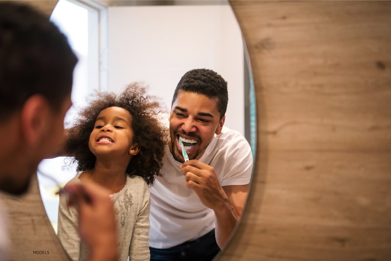 Father and daughter brushing their teeth together.