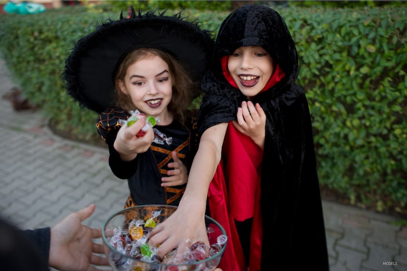 Two girls dressed as witches on Halloween, grabbing candy from bowl