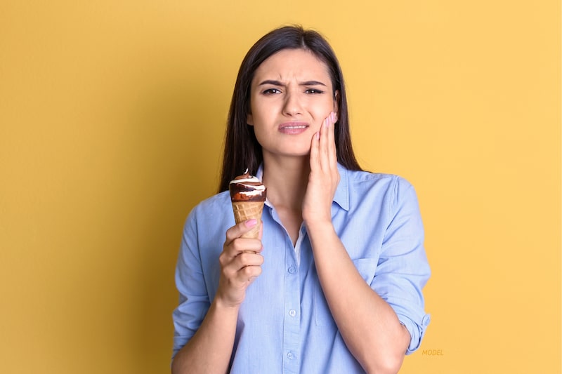 Woman with ice cream cone, touching her jaw due to a toothache.