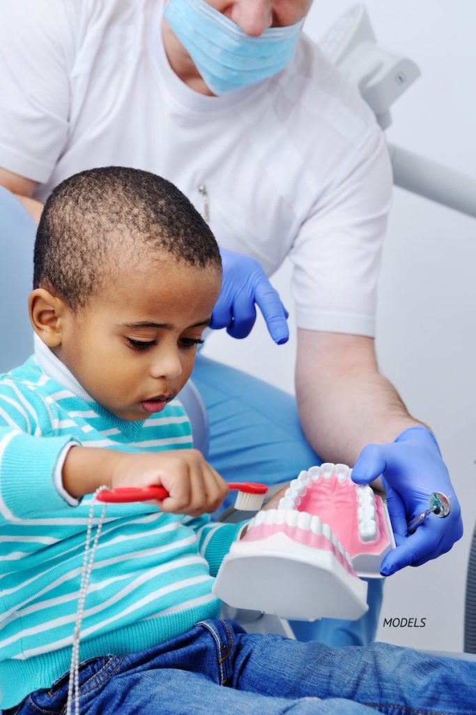 Young boy learning how to brush teeth at his dentist's office