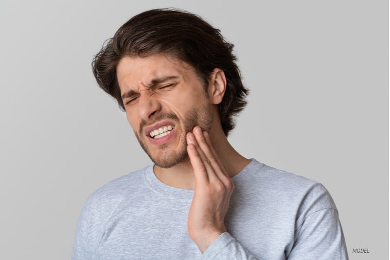 Man with tooth pain touching his jaw.