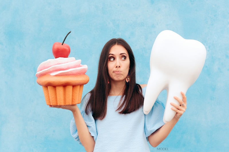 Woman holding up a giant cupcake in one hand and a giant tooth in the other.