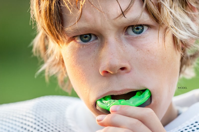 Young male athlete puts a sports mouth guard in his mouth.