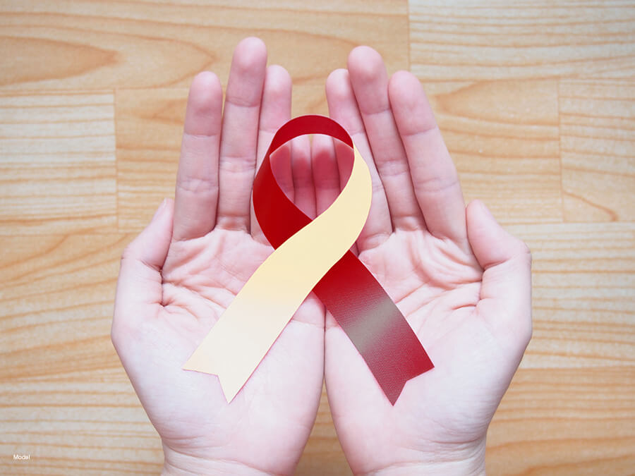 A close-up of two hands holding a burgundy and ivory ribbon to commemorate oral cancer.