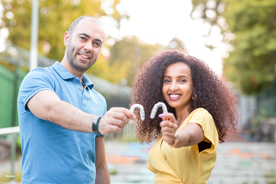 A man and woman with nice smiles hold up their clear dental aligners.